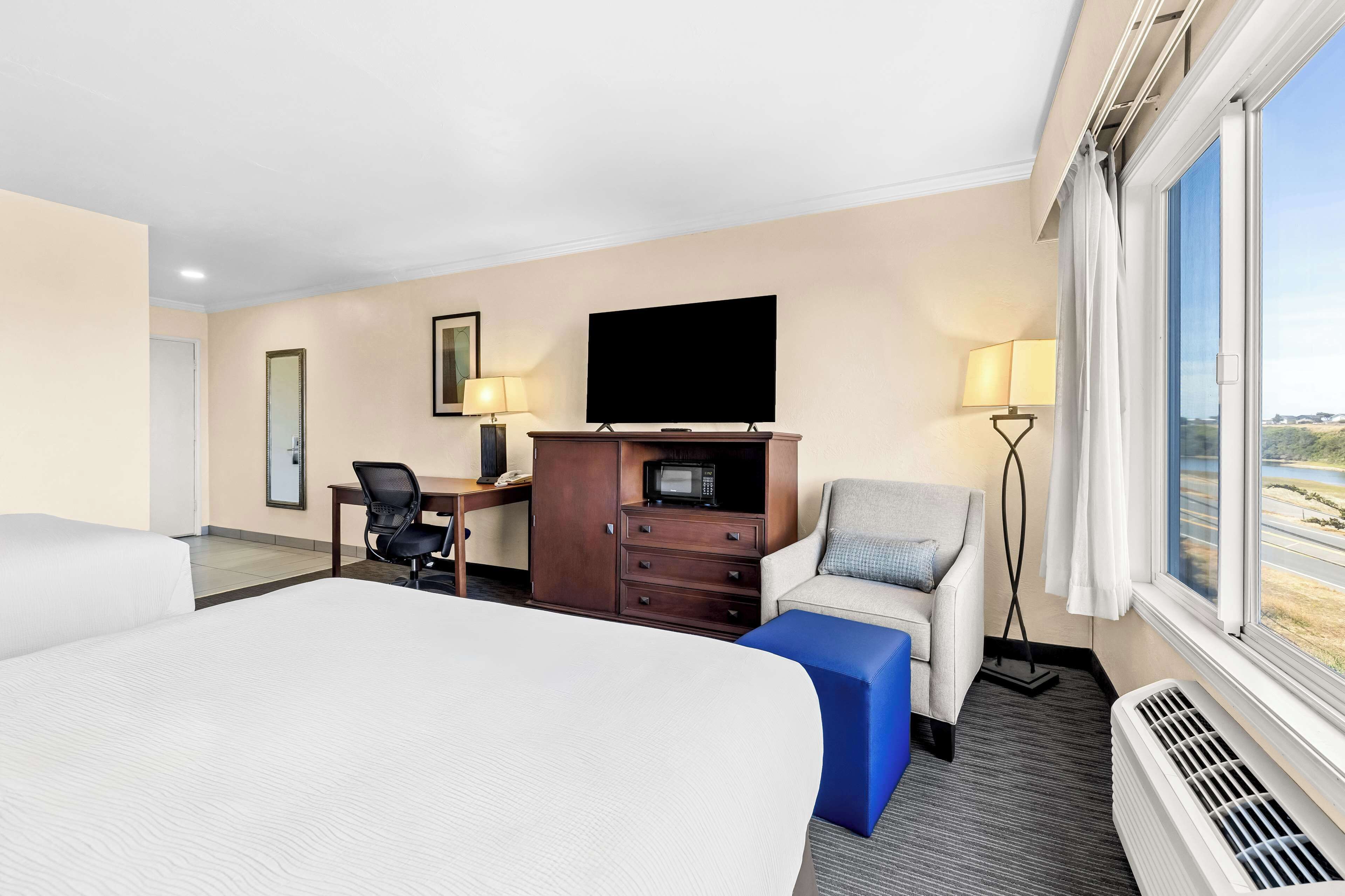 Una camera d'albergo con un letto, una scrivania con una sedia, una televisione, una lampada e vista sull'esterno.