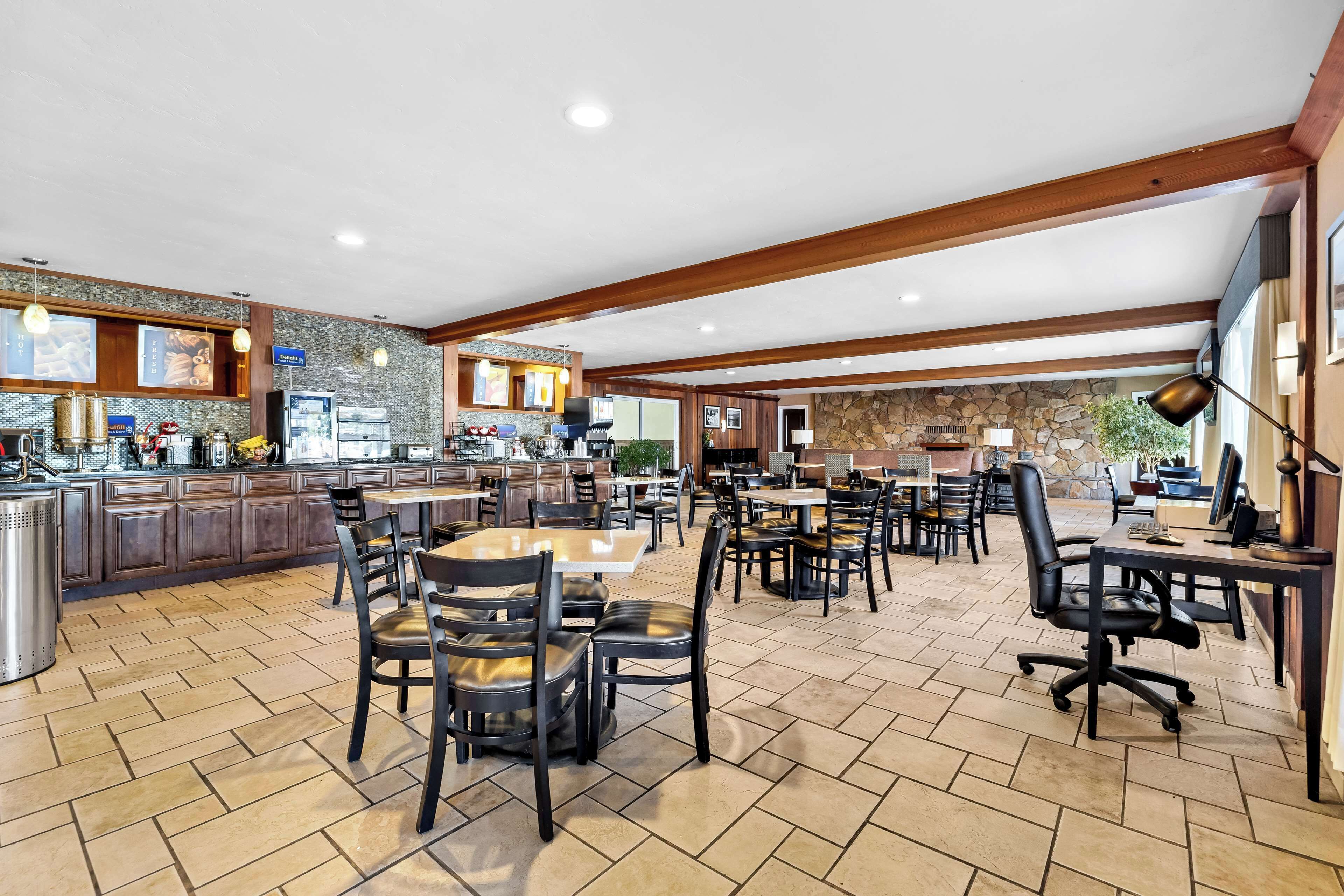 Un vaste espace de salle à manger avec plusieurs tables et chaises, un coin cuisine doté de plans de travail en granit et un mur en pierre en arrière-plan.
