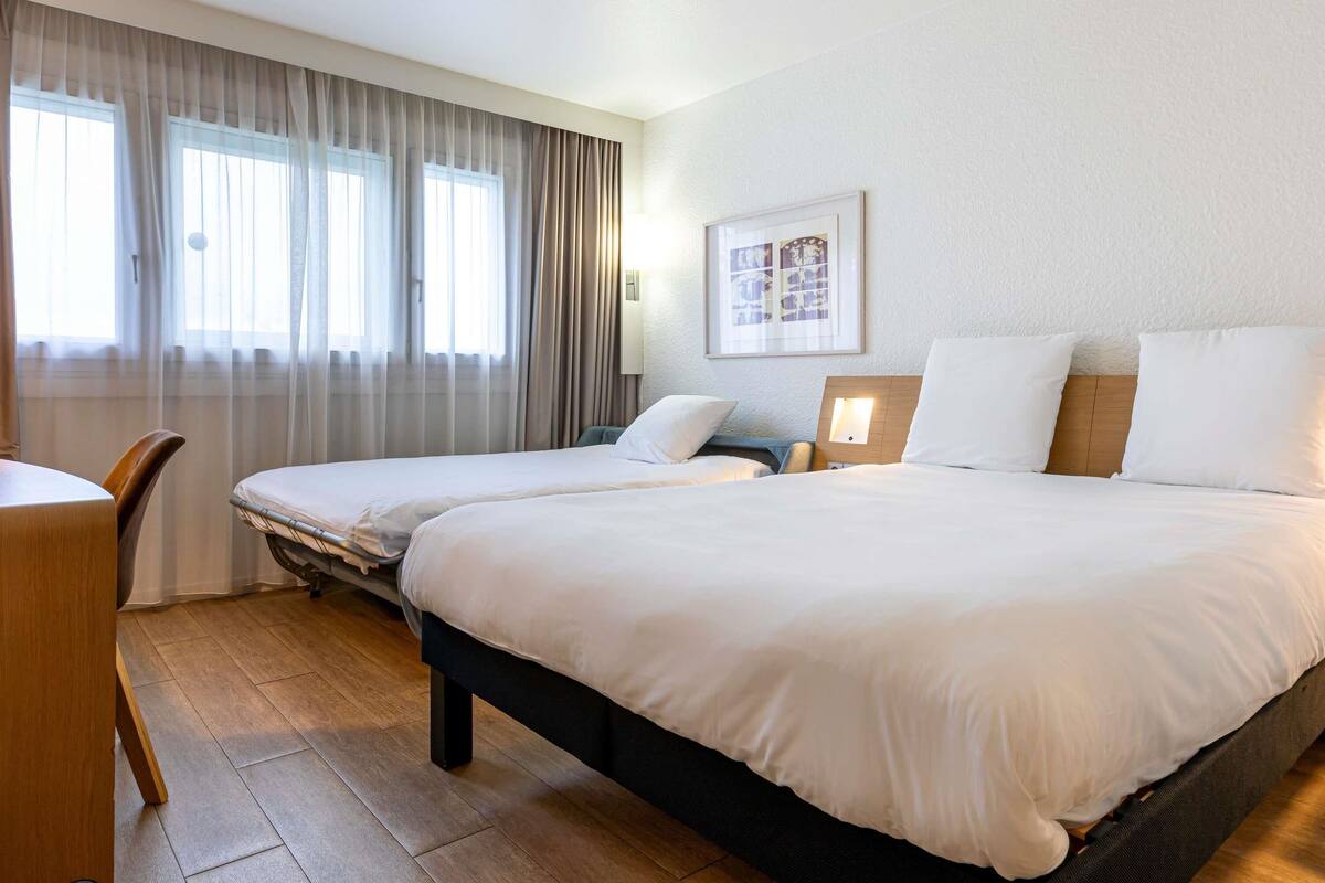 A hotel room with two beds, a desk, and a window with curtains.