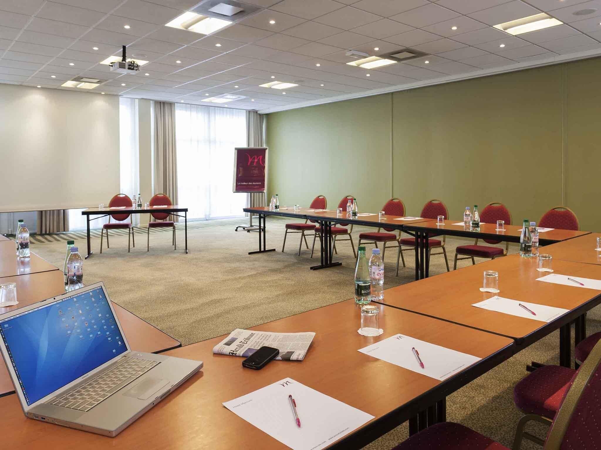 Une salle de conférence avec un ordinateur portable, des documents et des bouteilles d’eau sur les tables.