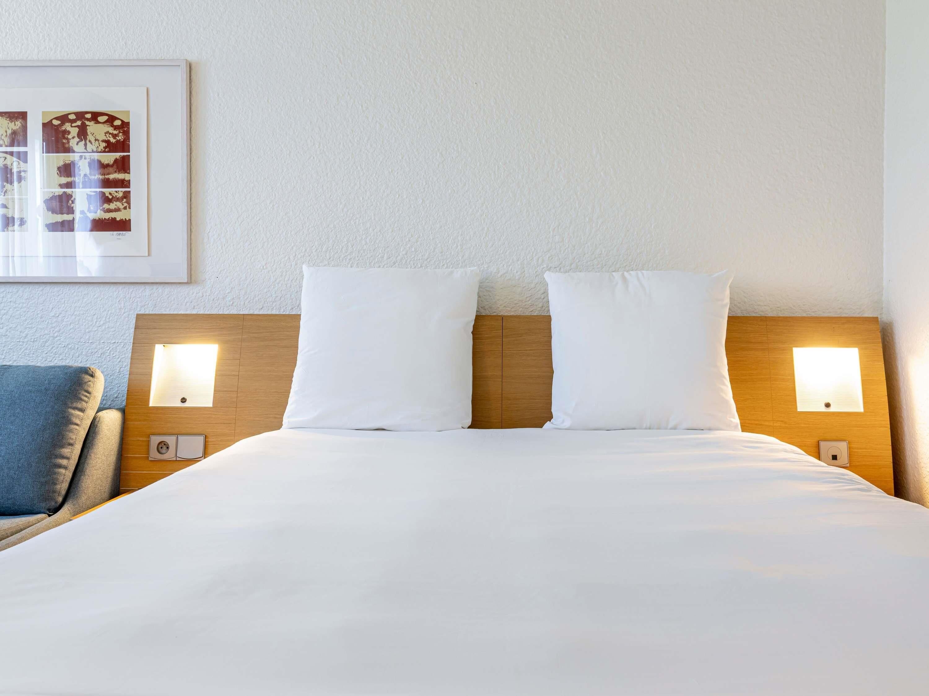 A hotel room with a large bed, two bedside tables with lamps, a framed picture on the wall, and a blue chair.