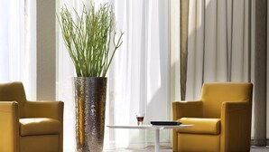 A room with two yellow armchairs, a white coffee table, and a large textured plant in a metallic vase. - Mercure Paris Le Bourget (Le Blanc-Mesnil)