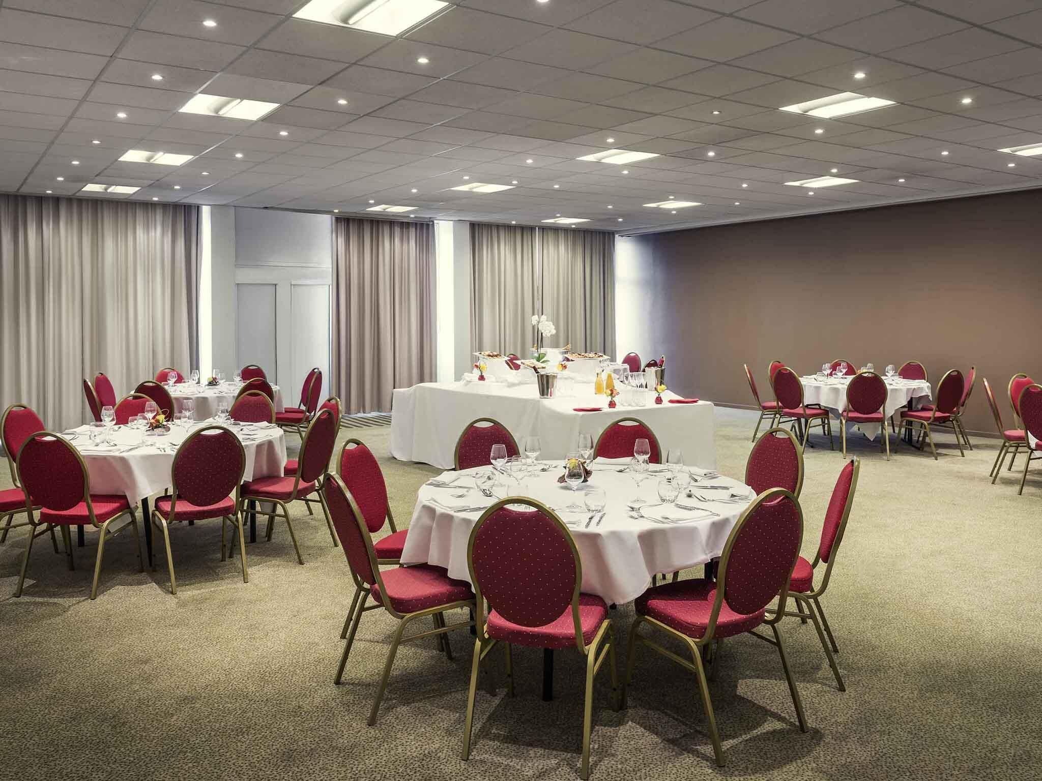 A conference room with round tables, red chairs, and a central table with a white tablecloth.