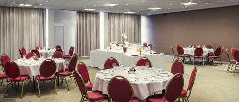 A conference room with round tables, red chairs, and a central table with a white tablecloth.