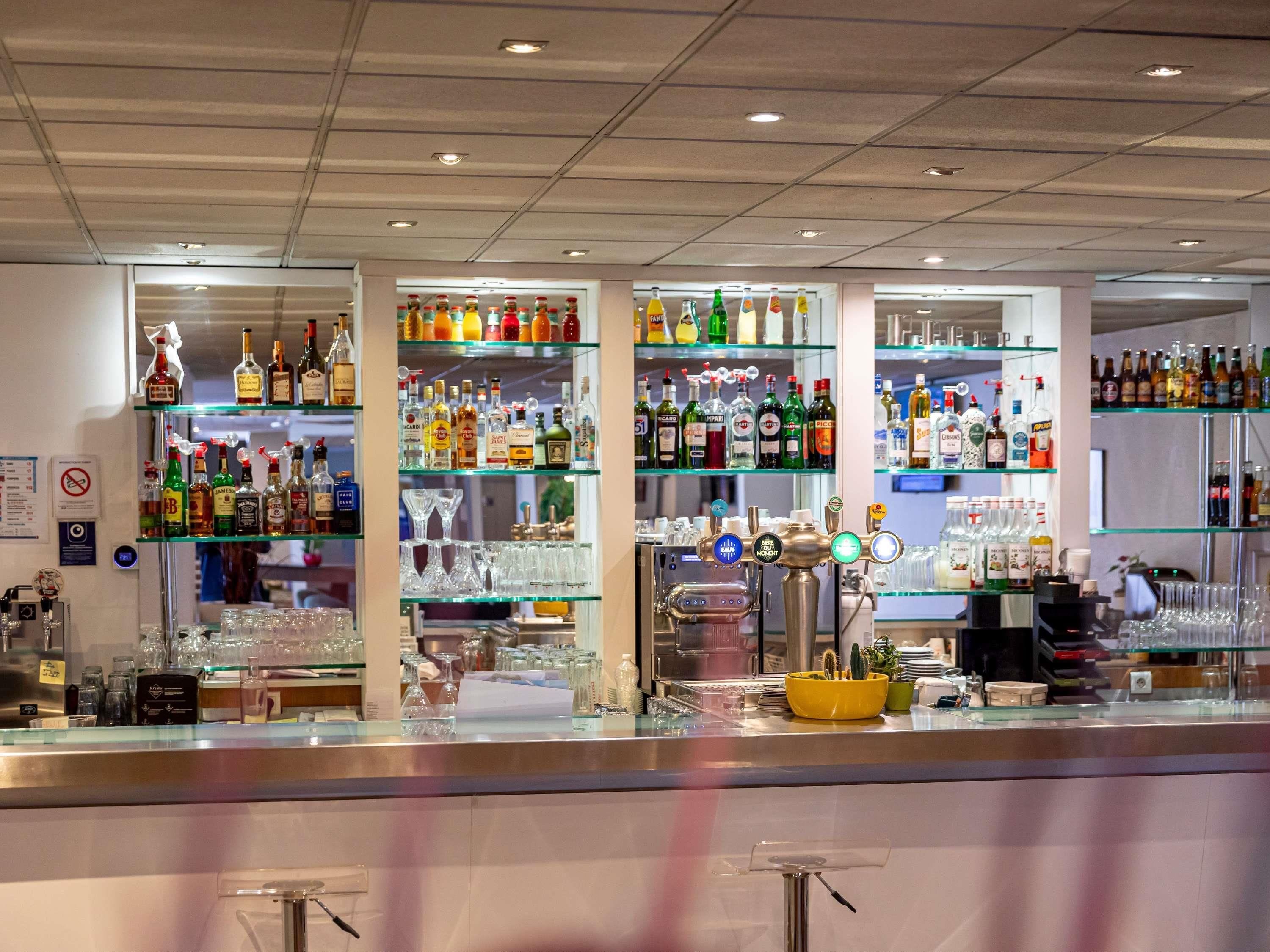 A bar with shelves of liquor bottles, glasses, and a bar counter with a cash register.
