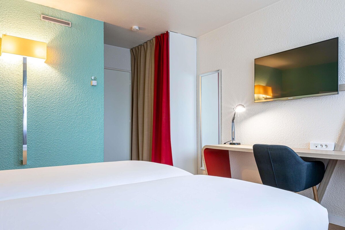 A hotel room with a bed, desk, chair, and a television mounted on the wall.