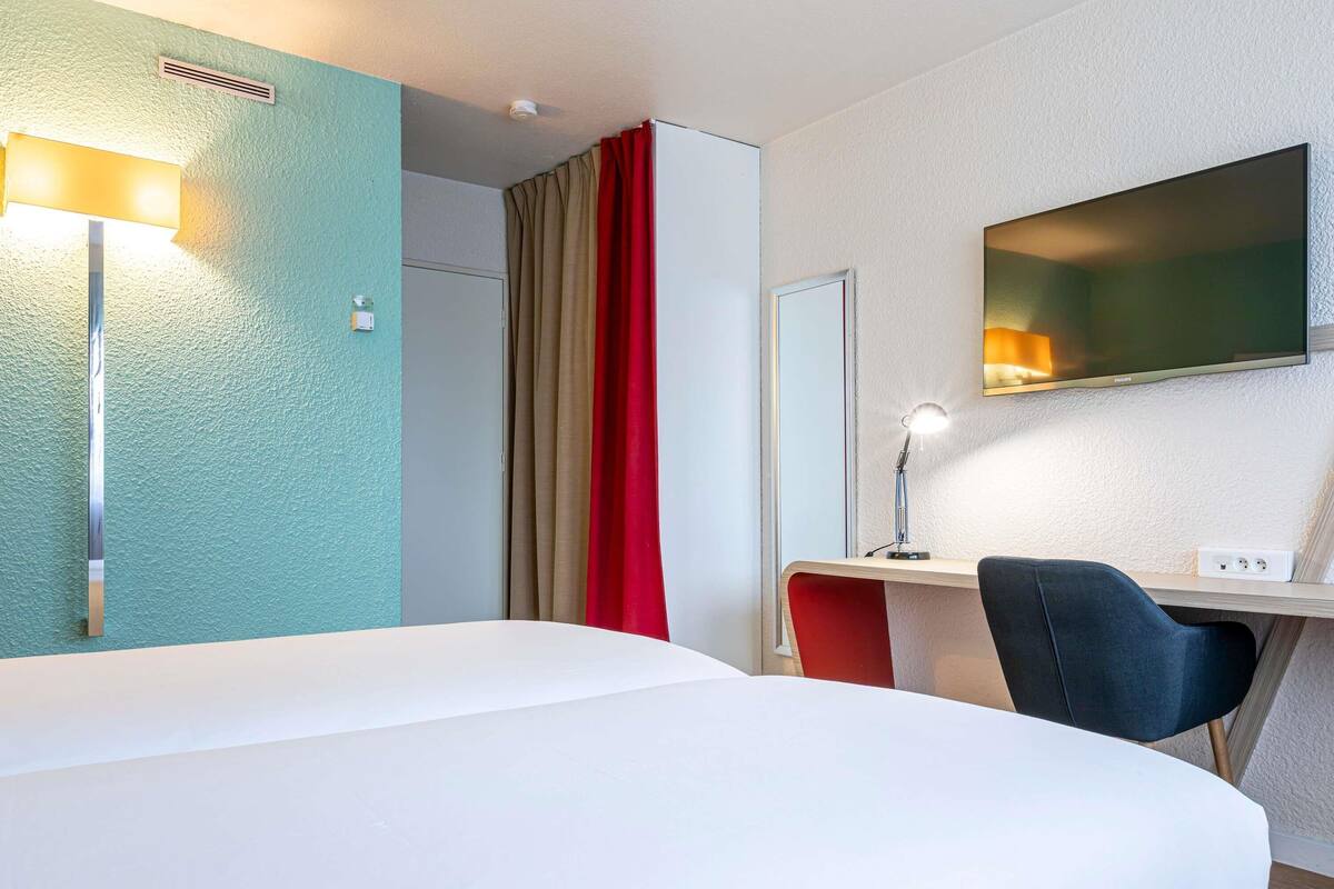 A hotel room with a bed, desk, chair, and a television mounted on the wall.