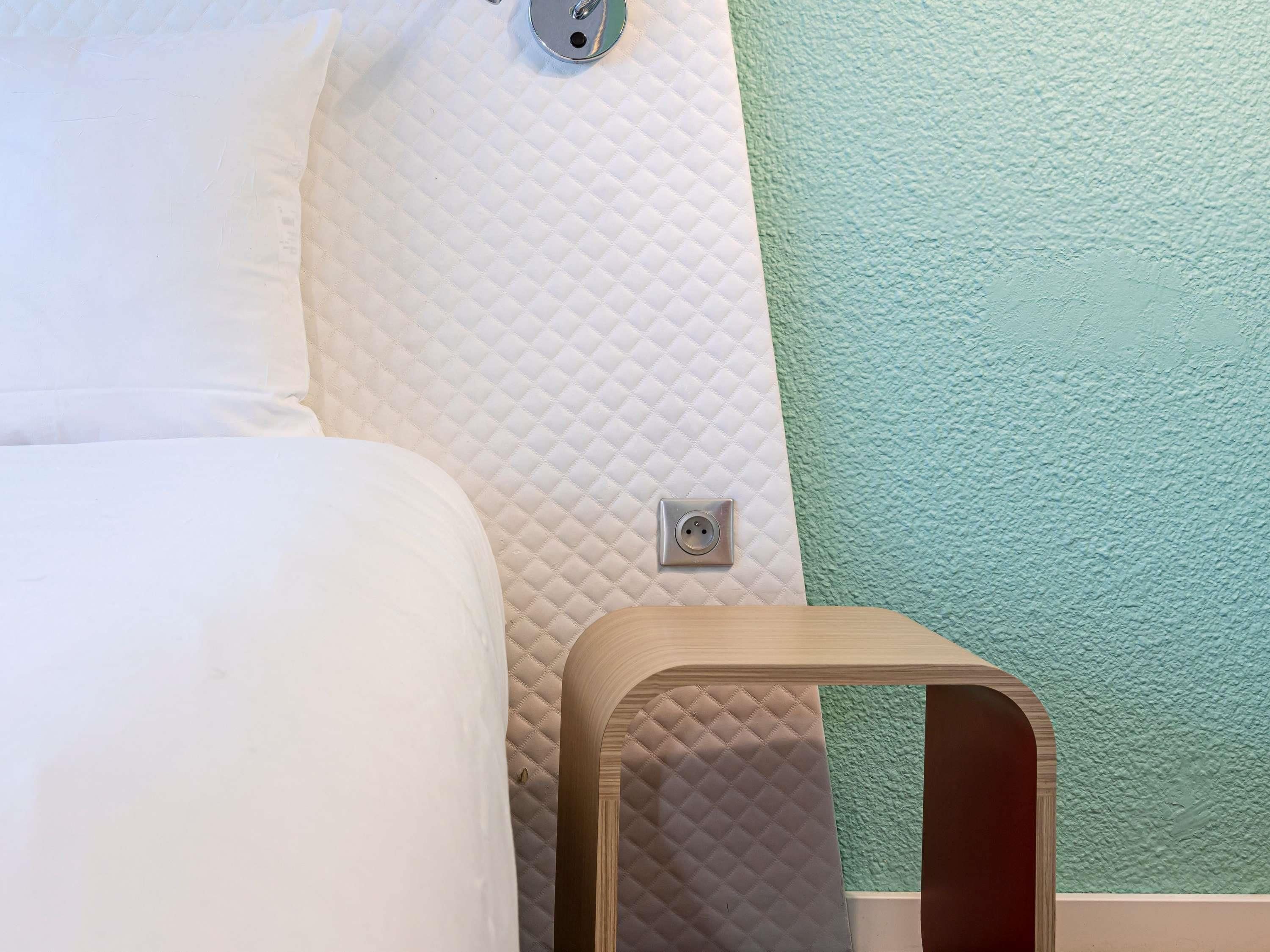 A bed with a quilted mattress, a wooden nightstand, and a wall socket.