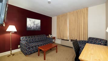 A furnished room with a sofa, a table, a lamp, and a window with curtains.