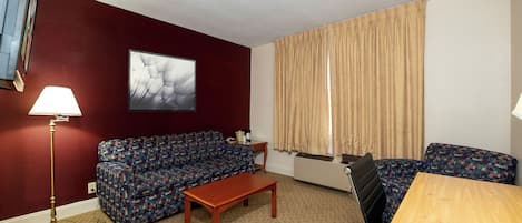 A furnished room with a sofa, a table, a lamp, and a window with curtains.