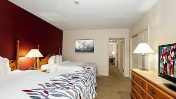 A hotel room with two beds, a television, a dresser, and a hallway leading to a door.