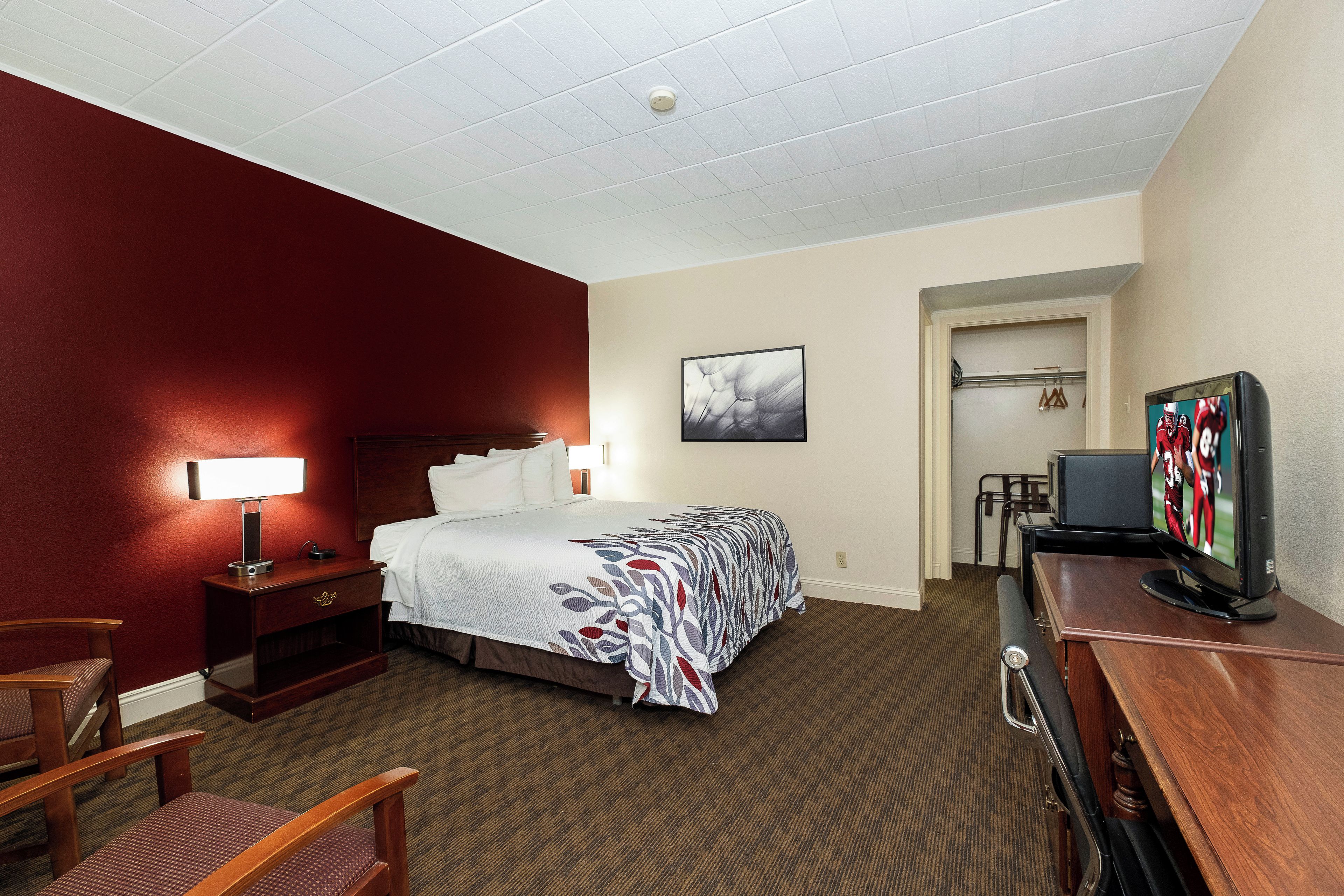 A hotel room with a bed, bedside table, lamp, TV, and a coat rack.