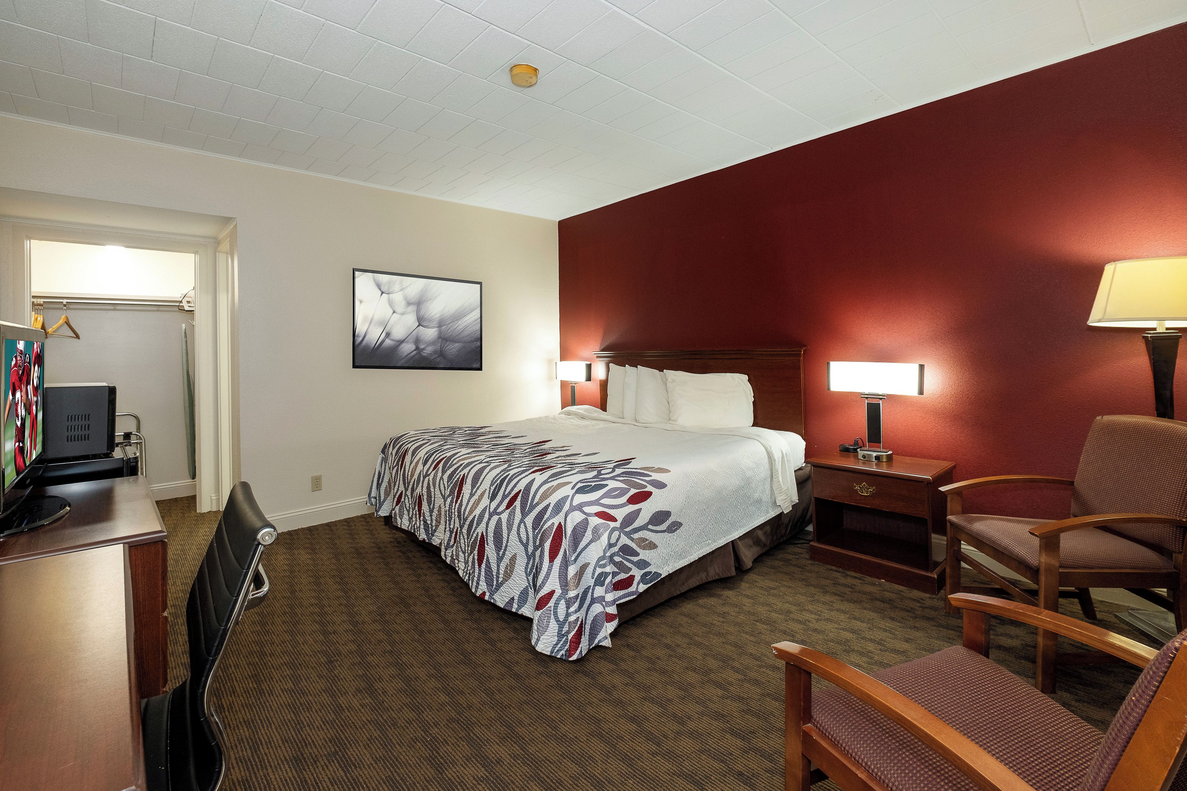 A hotel room with a bed, a desk with a computer, a chair, a lamp, and a painting on the wall.