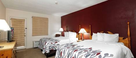 A hotel room with two beds, a desk with a television, and a window with blinds.