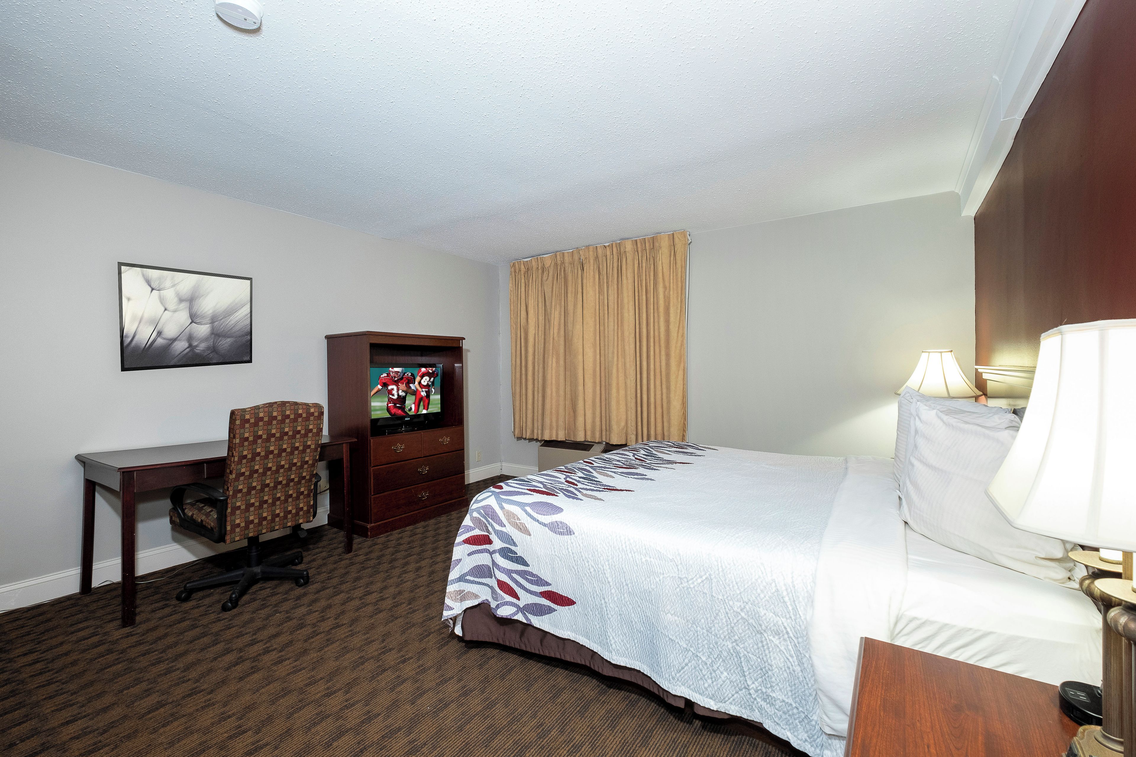 A hotel room with a bed, desk, chair, television, and a window with curtains.