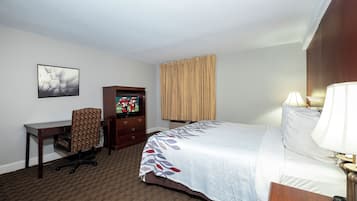 A hotel room with a bed, desk, chair, television, and a window with curtains.