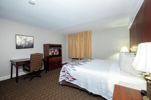 Habitación de hotel con cama, escritorio, silla, televisor y ventana con cortinas.