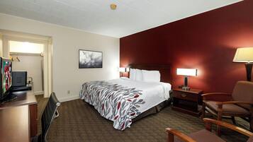 A hotel room with a bed, bedside tables, a desk with a computer, a chair, and a TV.