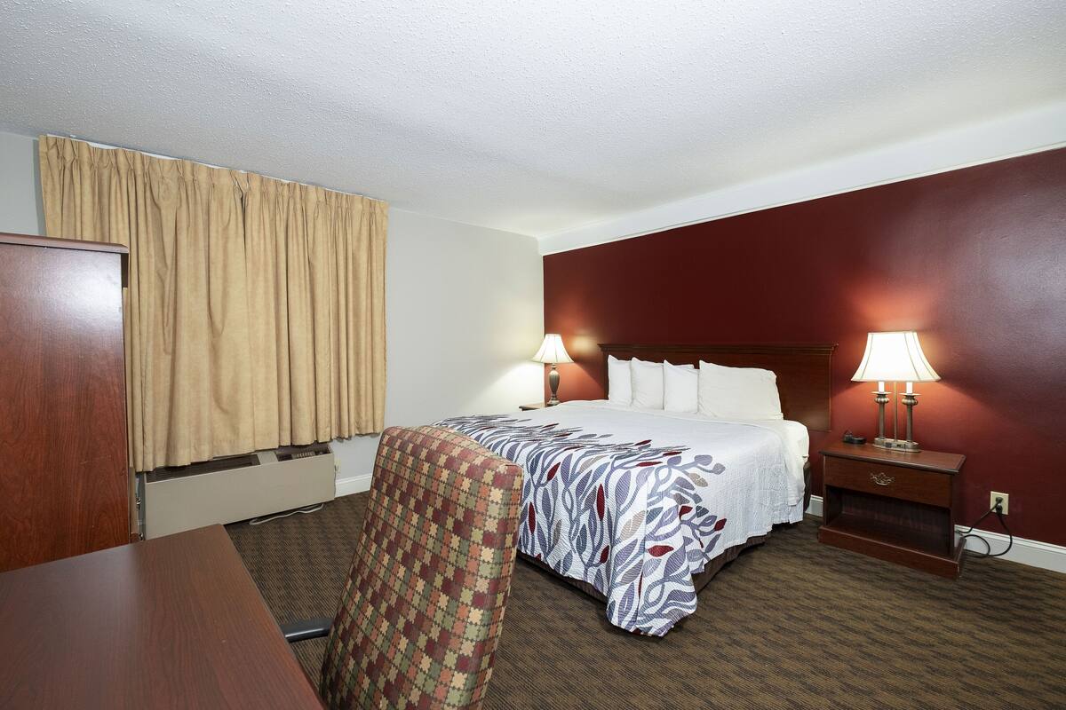 A hotel room with a bed, two bedside lamps, a desk, and a chair.