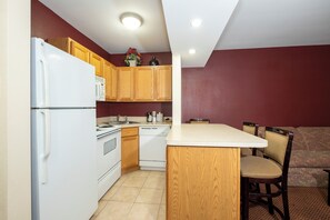 Una cucina compatta con mobili in legno, un frigorifero bianco, un fornello e una lavastoviglie. C'è un'area pranzo con un tavolo e sedie.