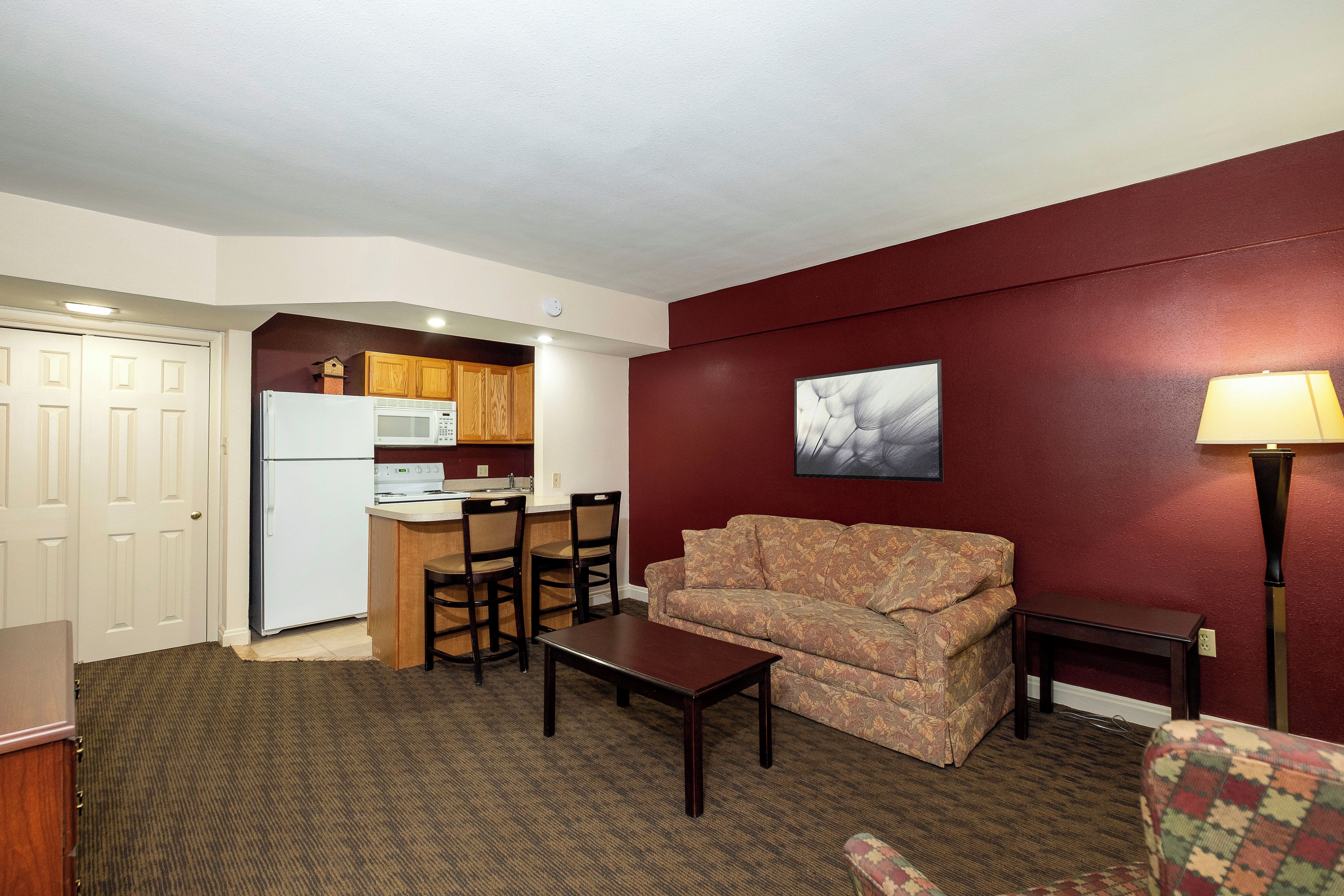 A compact living space with a kitchenette, a sofa, a coffee table, and a patterned armchair.