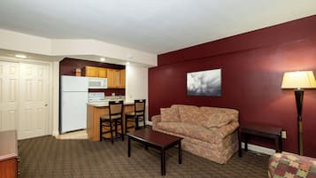 A compact living space with a kitchenette, a sofa, a coffee table, and a patterned armchair.