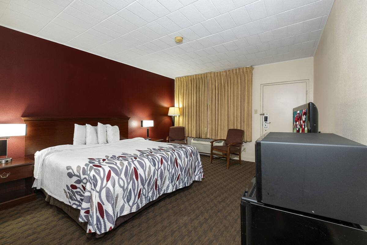 A hotel room with a large bed, a desk with a lamp, a TV, and a chair.
