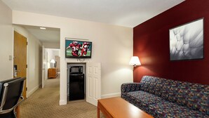 A hotel room with a television mounted on the wall, a sofa, a coffee table, a microwave, and a door leading to another room. - Red Roof Inn & Suites Hazleton (Hazleton)