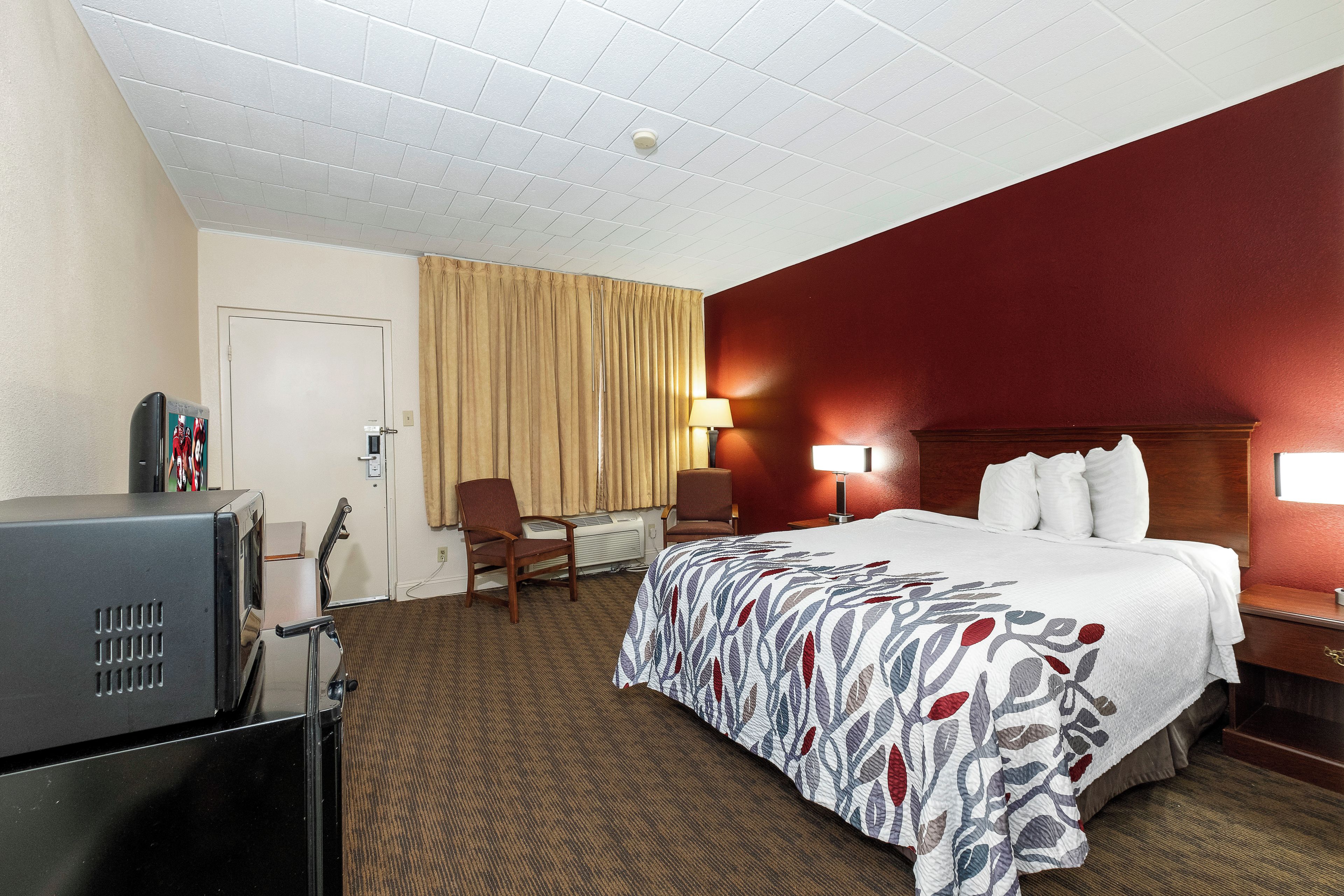 A hotel room with a bed, a desk, a chair, a television, and a window with curtains.