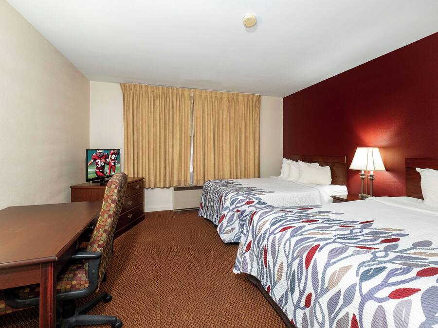 A hotel room with a bed, a desk, a chair, a television, and a lamp.