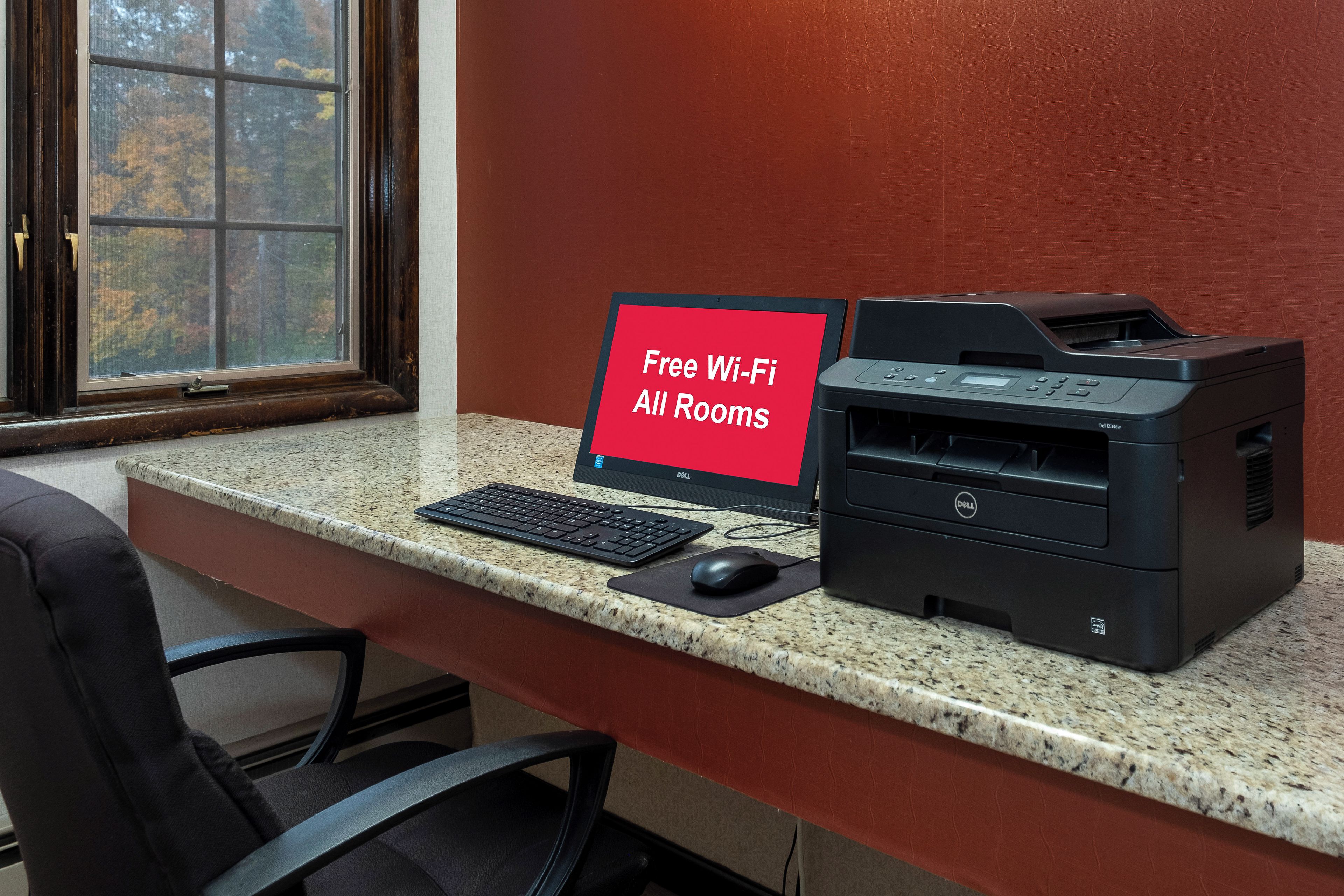A desk with a Dell computer, a printer, and a sign indicating free Wi-Fi in all rooms.