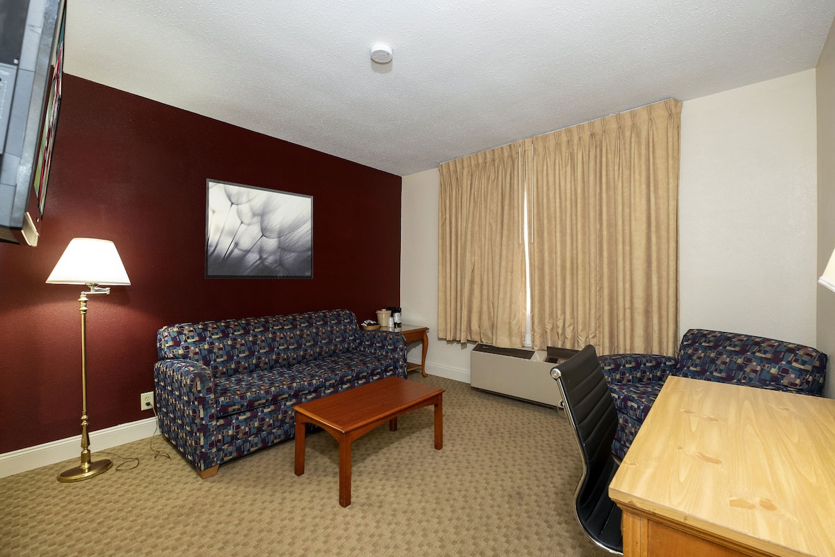 A living room with a sofa, a coffee table, a lamp, and a window with curtains.