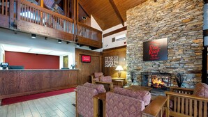 A hotel lobby with a stone wall, a fireplace, and a sign for Red Roof Inn & Suites. - Red Roof Inn & Suites Hazleton (Hazleton)