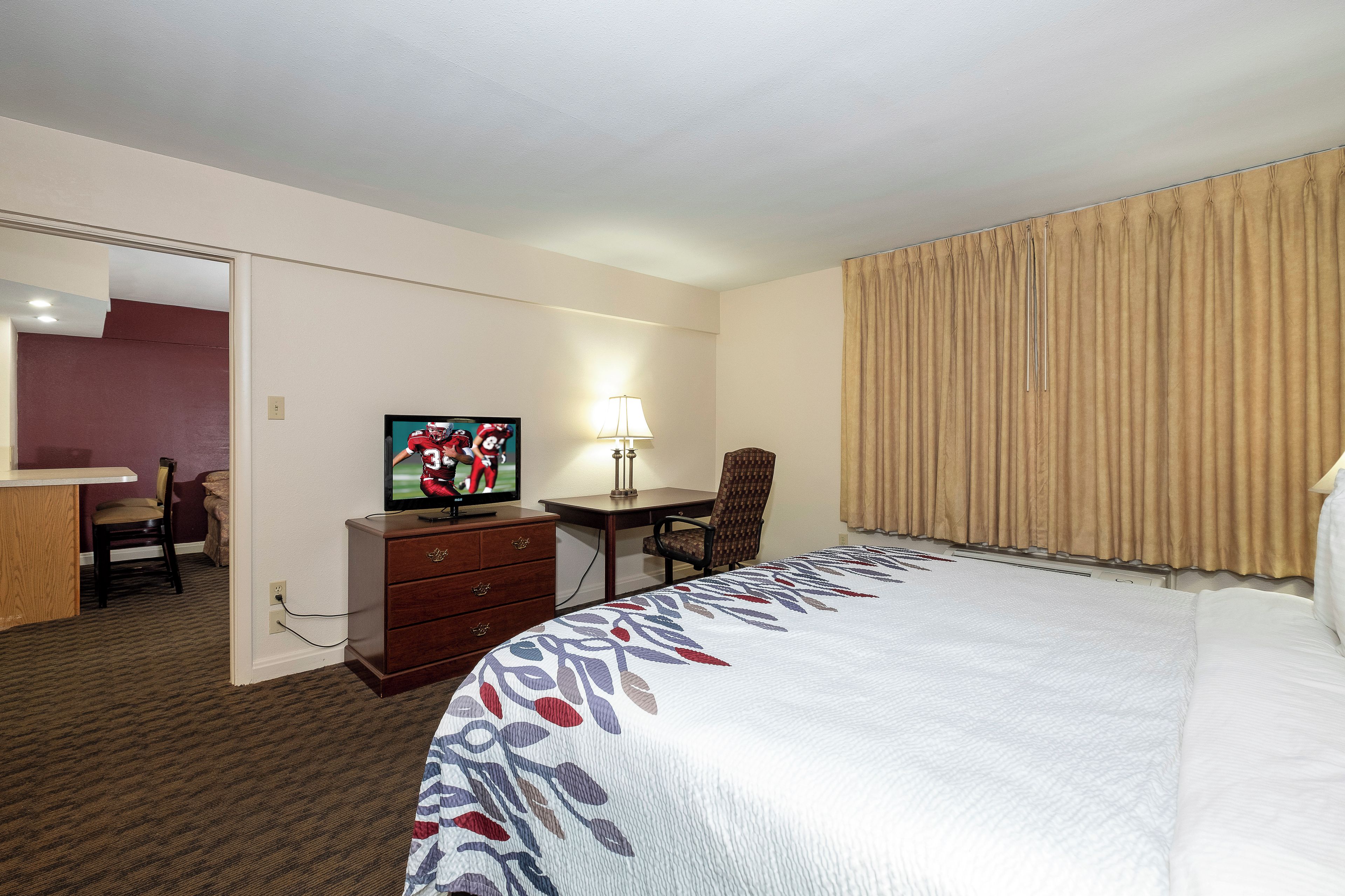 A hotel room with a bed, a desk, a chair, a television, and a mirror.