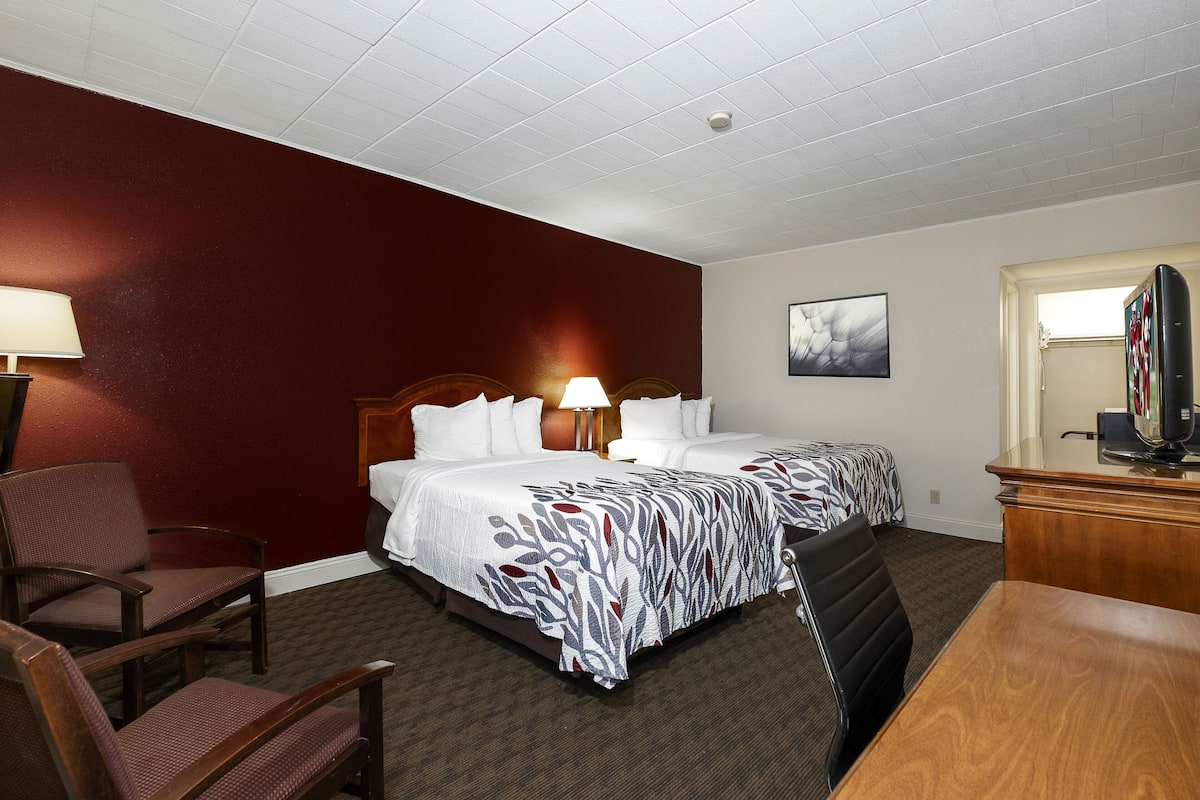 A hotel room with two beds, a desk, a chair, and a television.