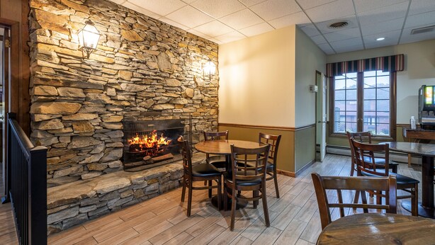A stone fireplace with a fire, surrounded by wooden chairs and a table in a dining area. - Red Roof Inn & Suites Hazleton (Hazleton)