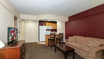 Un espacio habitable compacto con kitchenette, televisor, sofá y mesa de comedor.
