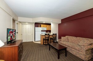 Un espacio habitable compacto con kitchenette, televisor, sofá y mesa de comedor.