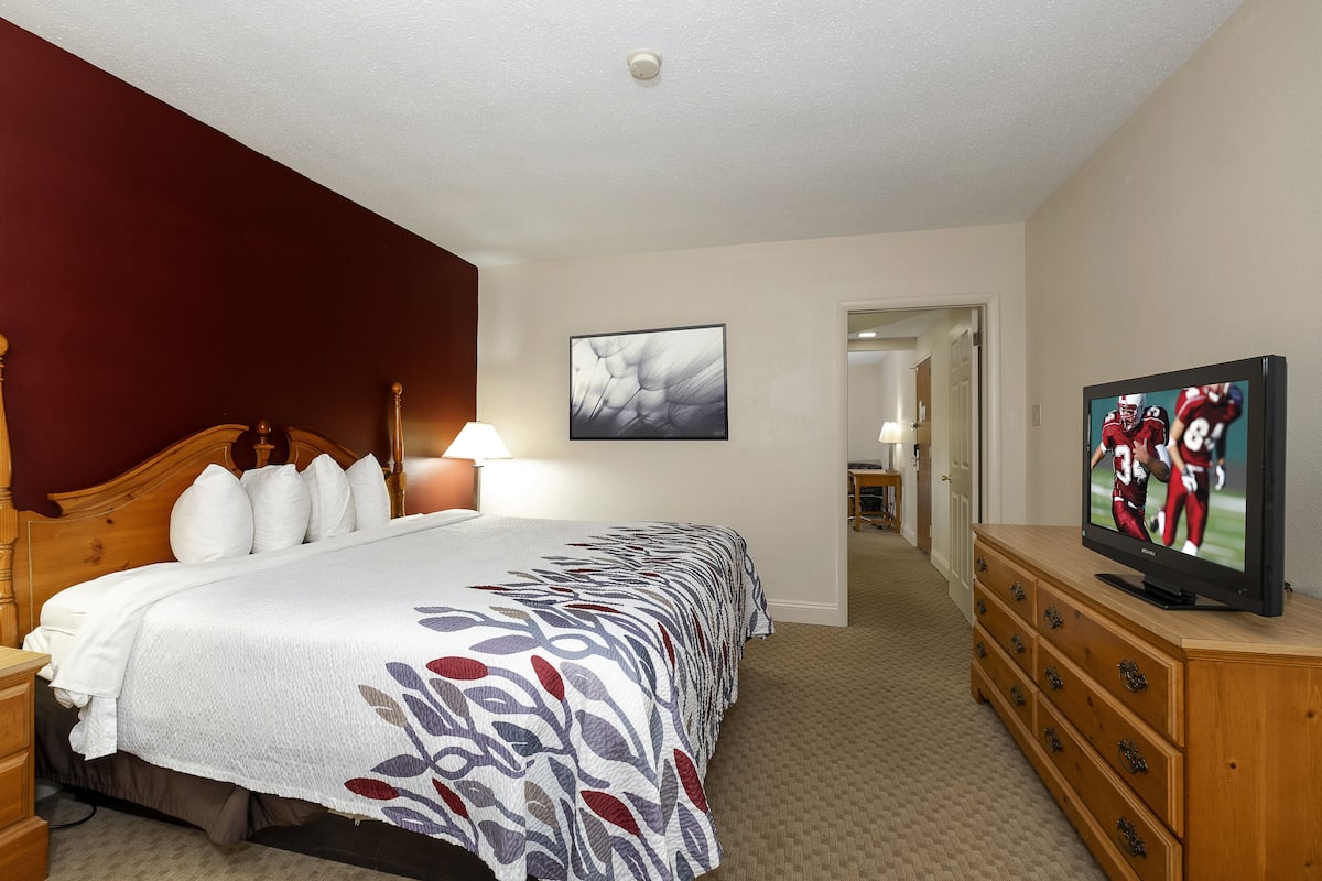 A hotel room with a large bed, a wooden dresser, a television, and a painting on the wall.
