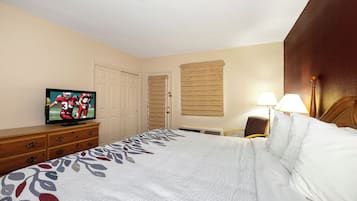 Habitación de hotel con una cama, un televisor sobre un mueble de madera, una puerta, una ventana con persianas y una lámpara.