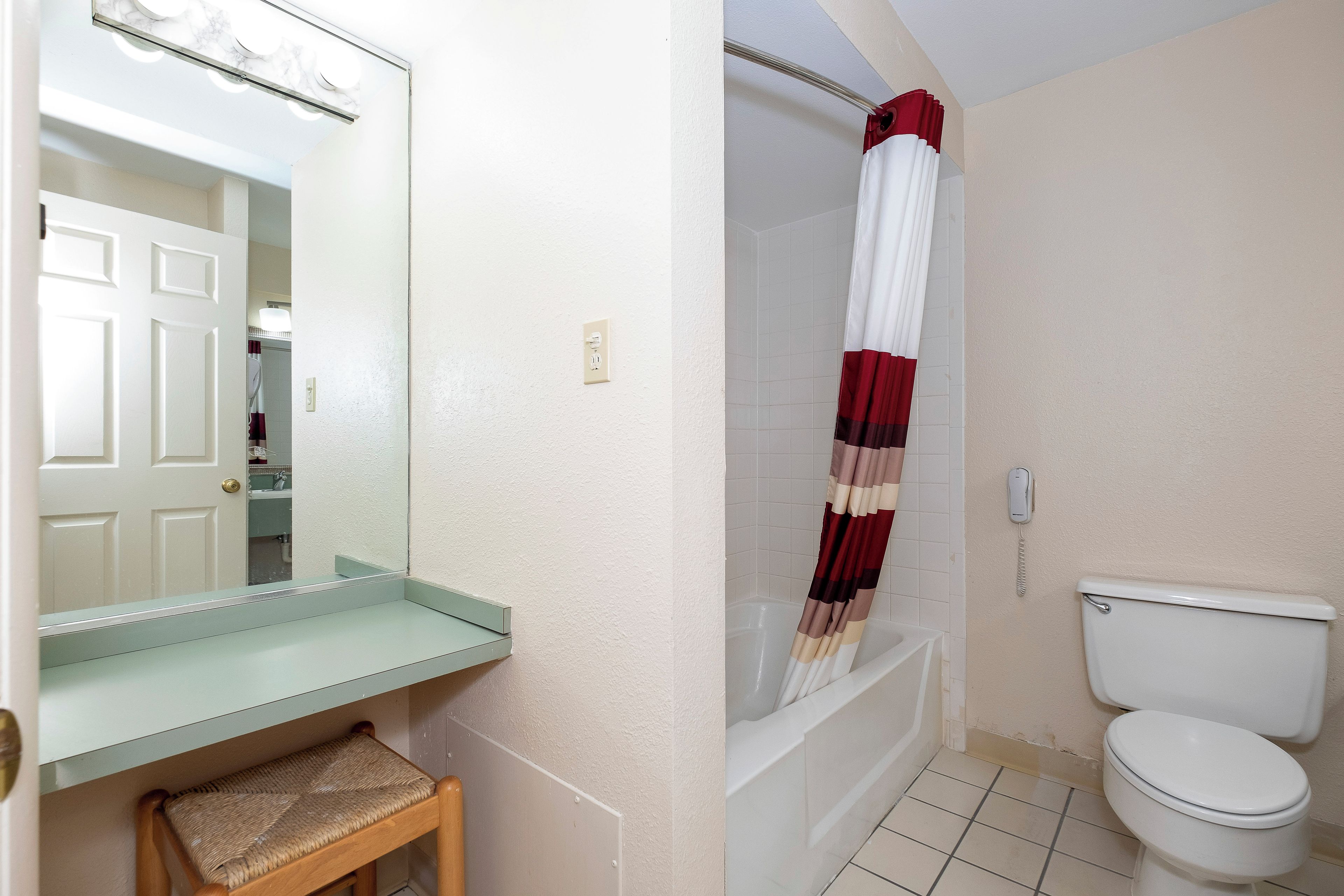 A bathroom with a toilet, a shower with a striped curtain, a mirror, and a small wooden stool.