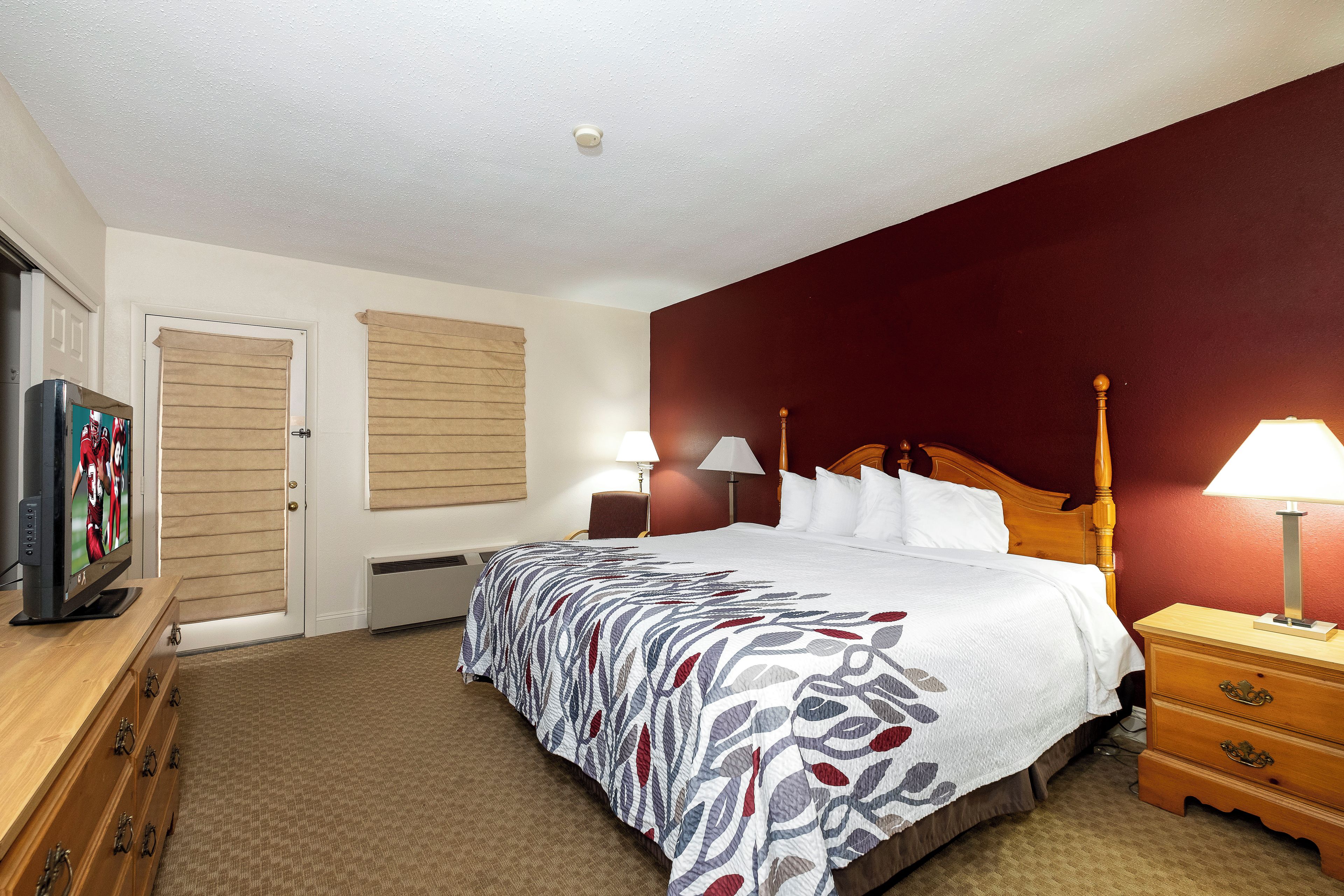 Een hotelkamer met een bed, een houten dressoir, een televisie en een raam met jaloezieën.