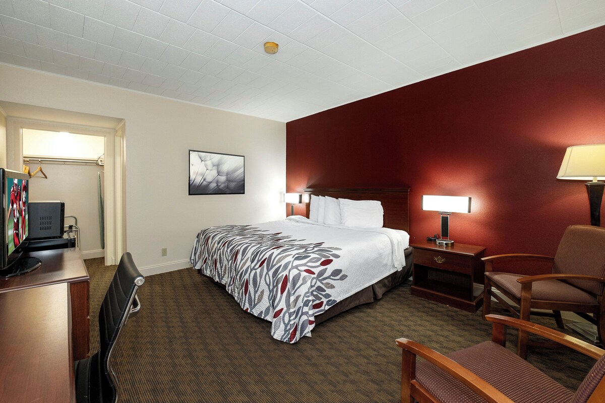 A hotel room with a bed, a desk with a computer, a chair, and a lamp.