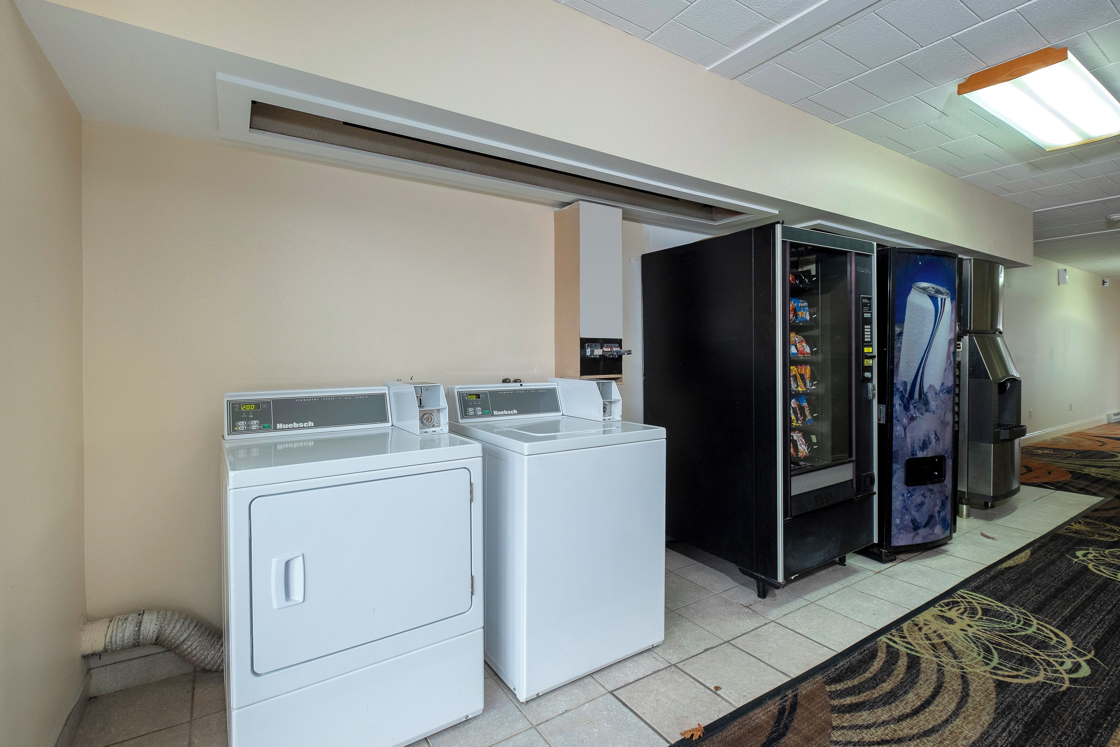A hotel laundry room with two front-loading washing machines, a vending machine, and a refrigerator.