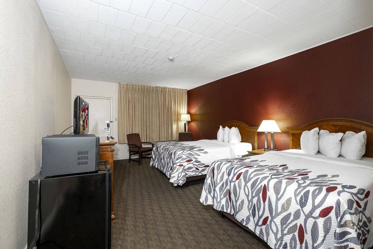 A hotel room with two beds, a desk, a television, and a window with curtains.