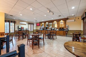 Un restaurante espacioso con varias mesas y sillas, una zona de bar y una pantalla digital con el menú.