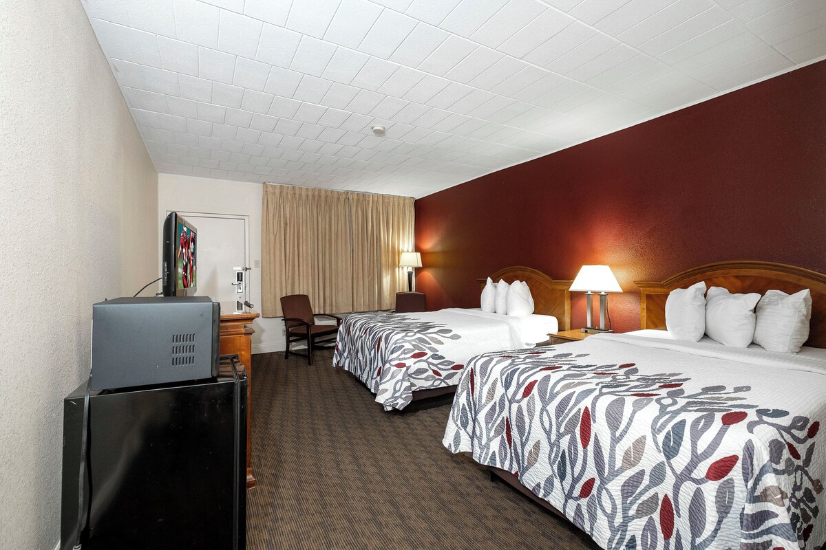 A hotel room with two beds, a desk, a television, and a window with curtains.