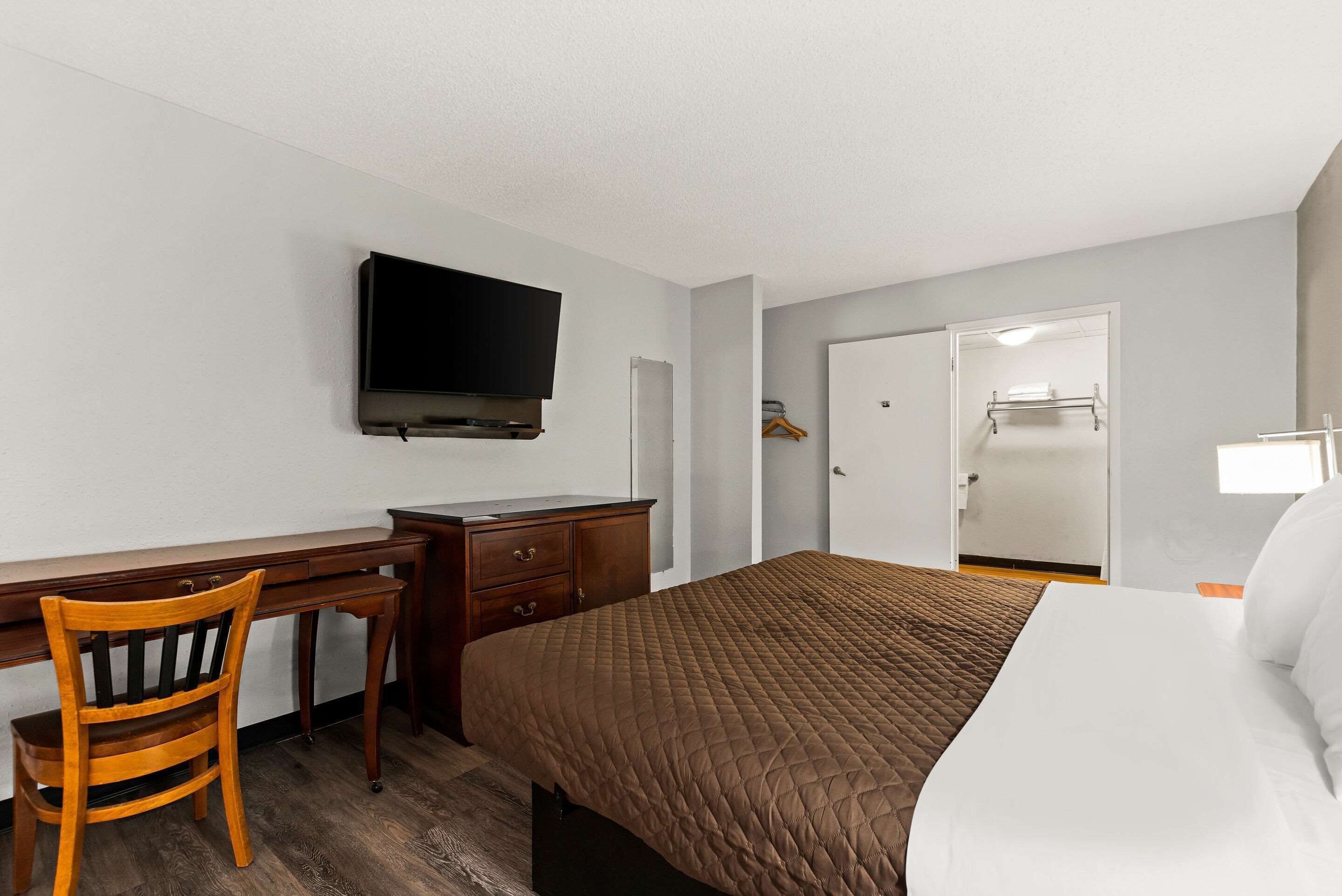 A hotel room with a bed, a desk, a chair, a television, and a wardrobe.