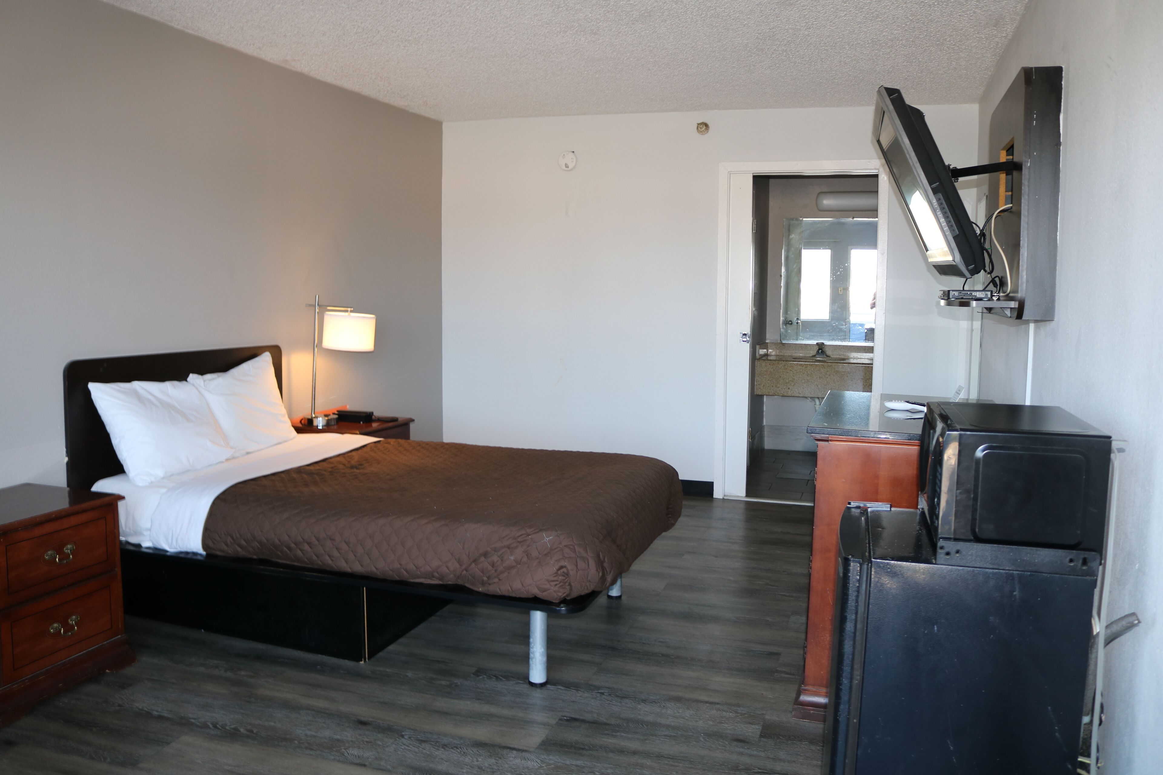 A hotel room with a bed, bedside table, lamp, and a TV mounted on the wall.