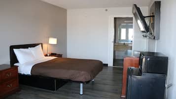 A hotel room with a bed, bedside table, lamp, and a TV mounted on the wall.